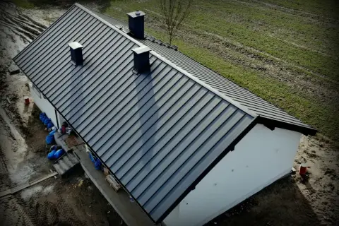 Nowy dach z blachy Budmat. Cennik dostępny online. Dom w trakcie budowy, otoczony zielenią.