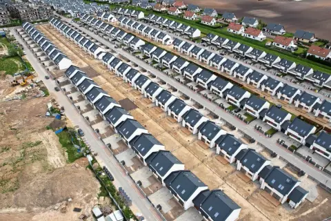Nowe osiedle domów jednorodzinnych, przykład suburbanizacji. Domy szeregowe z ciemnymi dachami i białymi elewacjami, otoczone placem budowy.