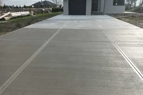 Nowy podjazd z beton stemplowany, z wyraźnymi liniami podziału, prowadzi do nowoczesnego domu.