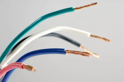 Pięć przewodów elektrycznych w różnych kolorach: zielonym, białym, czarnym, niebieskim i różowym, odsłaniających miedziane żyły. Różnorodne kolory faz.