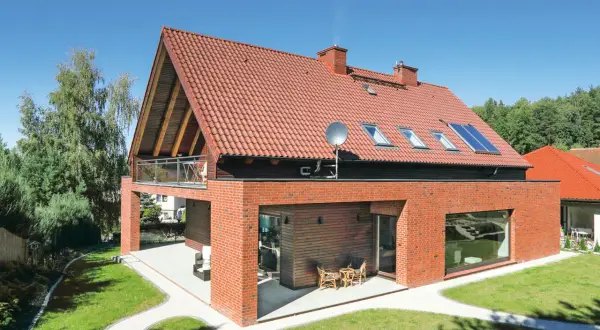 Nowoczesny dom z czerwonej cegły i dach dwuspadowy 100m2. Wokół zadbany ogród i drzewa.