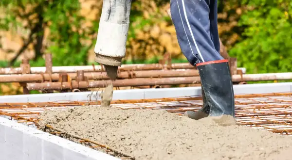 Beton c25/30 wylewany z pompy na zbrojenie. Pracownik w gumowcach stoi w świeżym betonie.