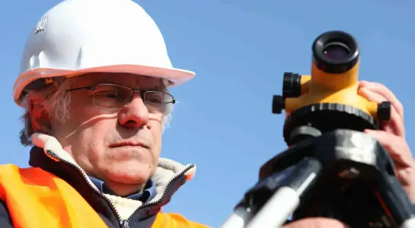 Geodeta w kasku i kamizelce odblaskowej pracuje z niwelatorem. Zastanawiasz się, ile kosztuje geodeta?
