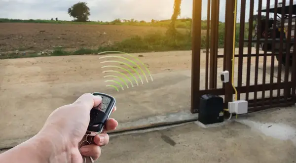 Programowanie pilota do bramy wjazdowej. Dłoń trzymająca pilot, z którego wychodzą zielone fale sygnału.