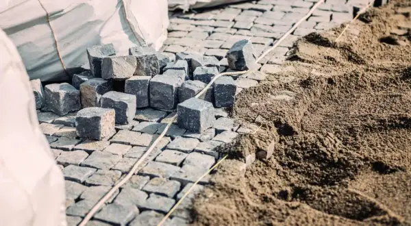 Kostka brukowa i piasek na budowie. Widać stosy kostki i przygotowany pod nią piasek, co sugeruje, ile podsypki pod kostkę na m2 jest potrzebne.