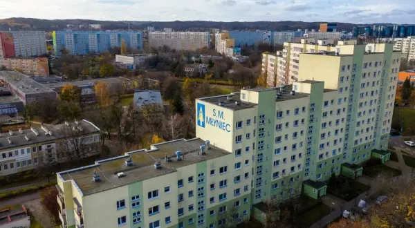 Osiedle bloków z wielkiej płyty S.M. Młyniec w jesiennej scenerii. Długie, wielopiętrowe budynki mieszkalne dominują w krajobrazie.