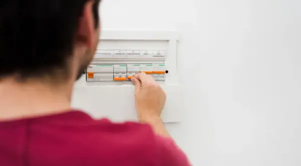 Mężczyzna manipuluje wyłącznikami w skrzynce elektrycznej, co może być pierwszym krokiem, by dowiedzieć się, jak obliczyć zużycie prądu.