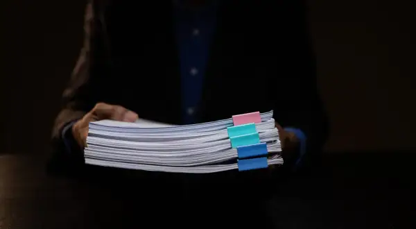Osoba w garniturze trzyma stos dokumentów z kolorowymi spinaczami, wśród których znajduje się wniosek o wykreślenie hipoteki.