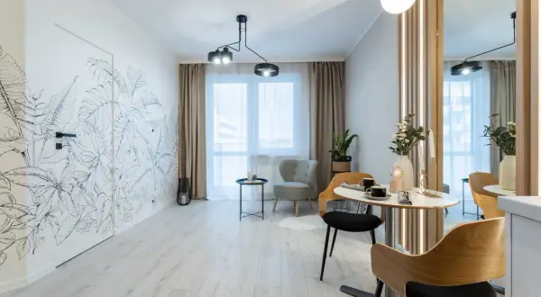 Nowoczesny salon z motywem roślinnym na ścianie. Wygodne fotele i stolik kawowy tworzą przytulną przestrzeń, idealną do relaksu. To wnętrze z rynku wtórnego zachwyca stylem.