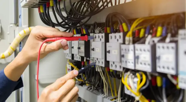 Elektryk sprawdza przewody w szafie sterowniczej. Widać multimetr i liczne kable, w tym przewód neutralny.