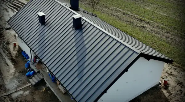 Nowy dach z blachy Budmat. Cennik dostępny online. Dom w trakcie budowy, otoczony zielenią.