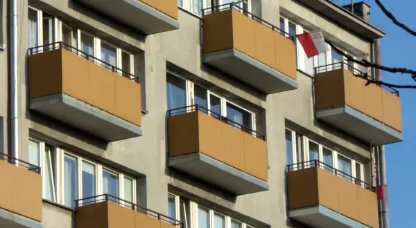 Szukasz informacji, jak dostać mieszkanie komunalne w Łodzi? Zobacz fasadę bloku z żółtymi balkonami i polską flagą.