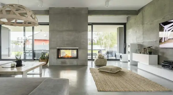 Nowoczesny salon z kominkiem i podłogą z betonu architektonicznego. To właśnie mikrocement nadaje wnętrzu surowego, ale eleganckiego charakteru.