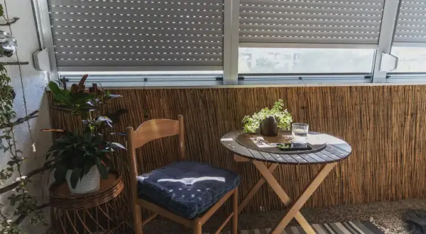 Przytulny balkon typu loggia z drewnianym krzesłem, stolikiem i roślinami. Idealne miejsce na poranną kawę.