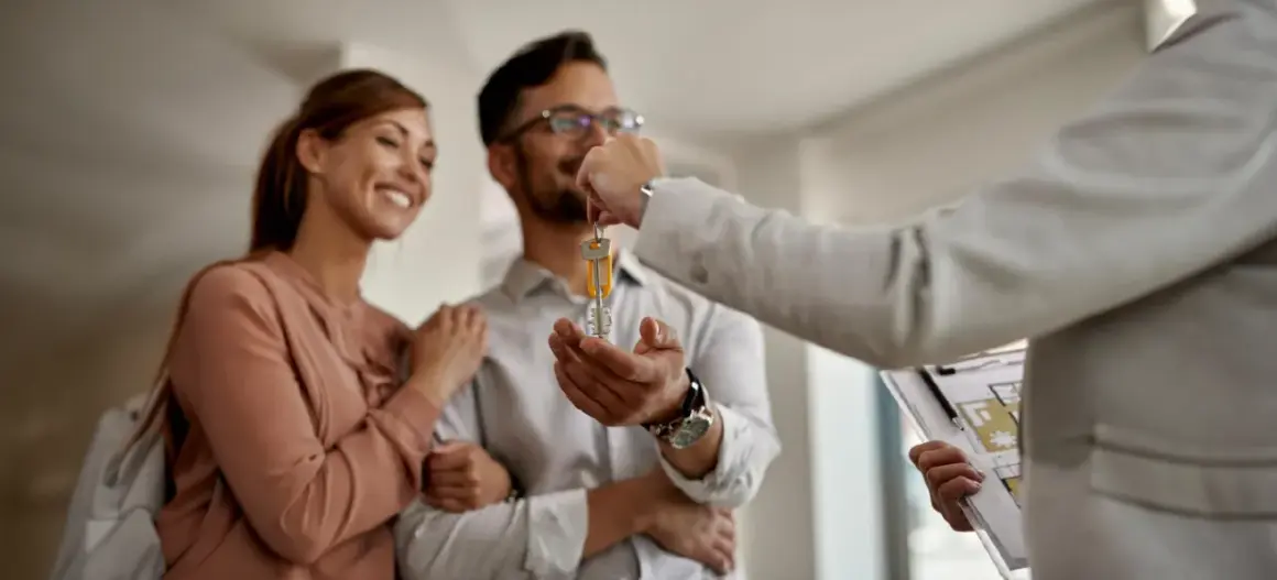 Szczęśliwa para odbiera klucze do nowego mieszkania. To symboliczny moment, który często towarzyszy inwestycjom w najem instytucjonalny.