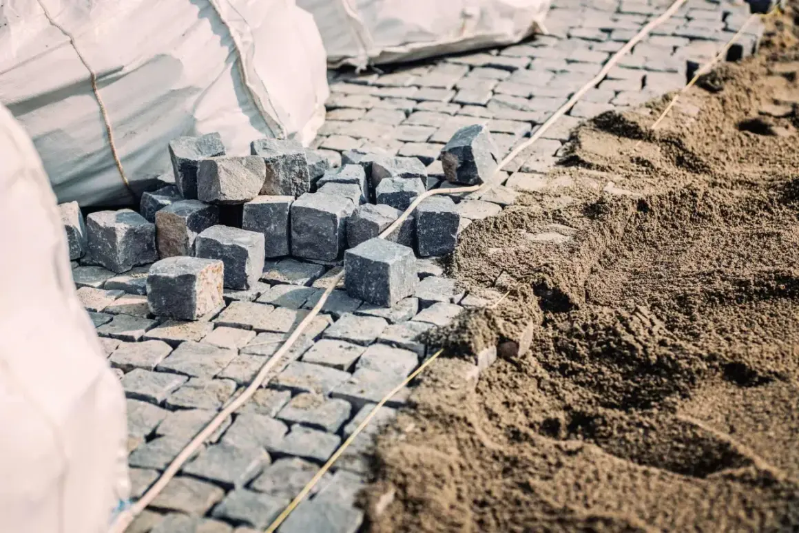 Kostka brukowa i piasek na budowie. Widać stosy kostki i przygotowany pod nią piasek, co sugeruje, ile podsypki pod kostkę na m2 jest potrzebne.