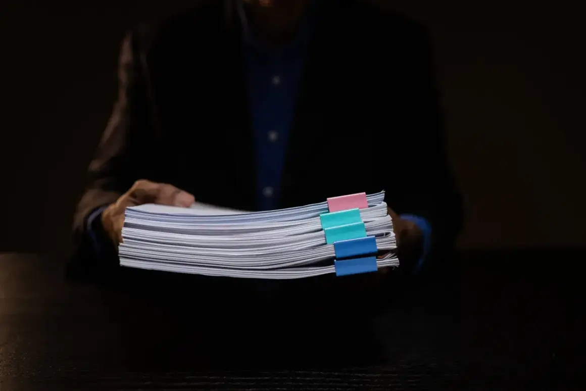 Osoba w garniturze trzyma stos dokumentów z kolorowymi spinaczami, wśród których znajduje się wniosek o wykreślenie hipoteki.
