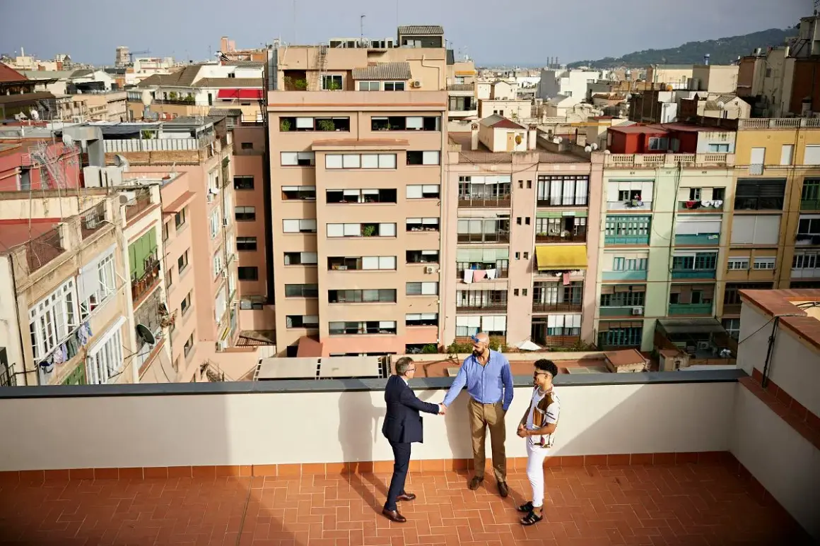 Trzech mężczyzn na dachu, w tle kolorowe kamienice. Rozmawiają o tanich mieszkaniach w Hiszpanii.