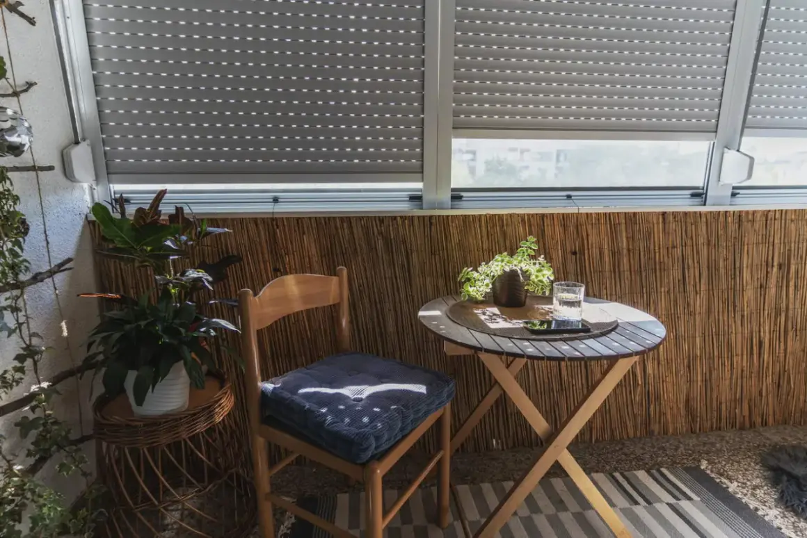 Przytulny balkon typu loggia z drewnianym krzesłem, stolikiem i roślinami. Idealne miejsce na poranną kawę.