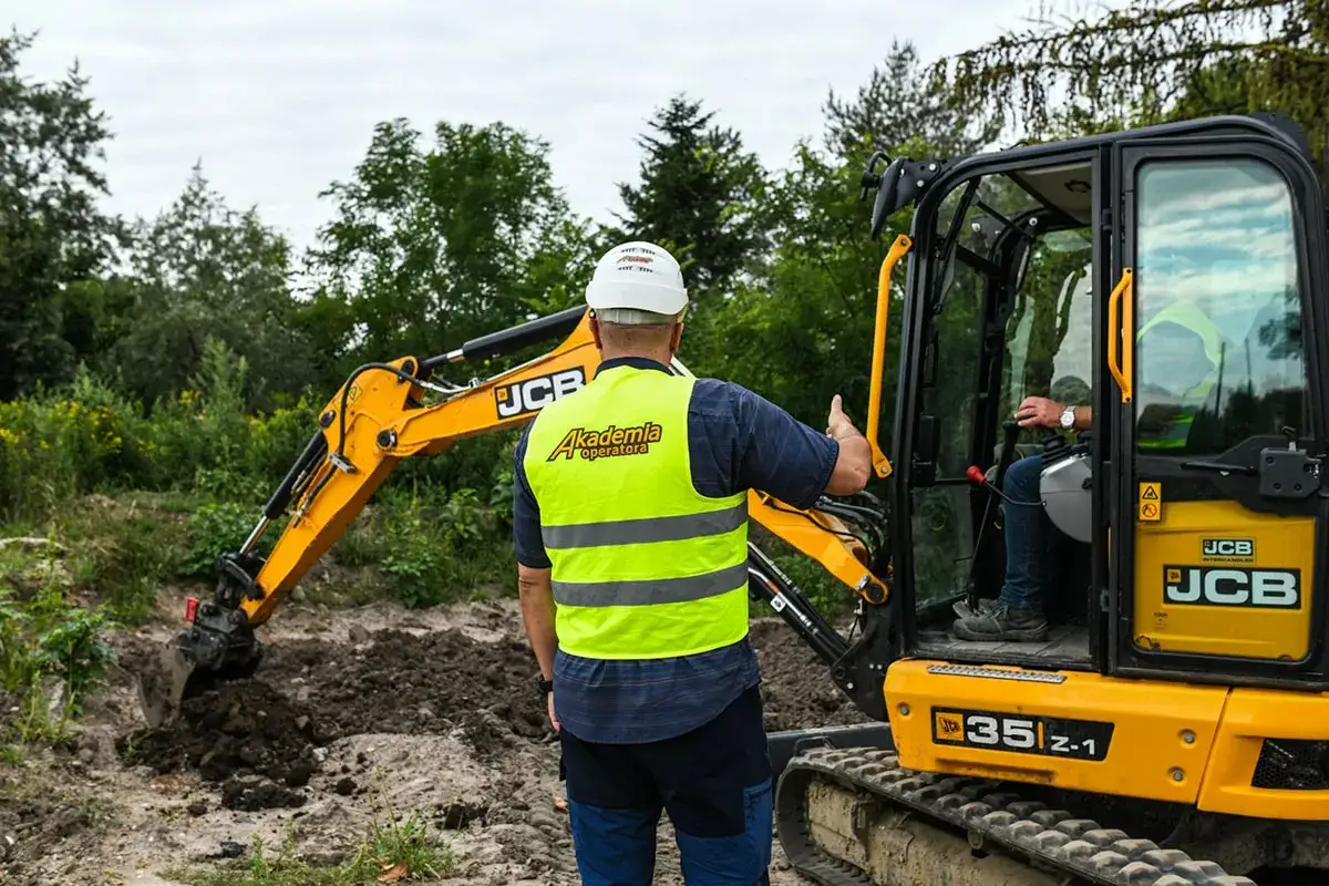 Operator w kamizelce odblaskowej instruuje kierowcę koparki. Zastanawiasz się, ile kosztuje godzina pracy koparki?