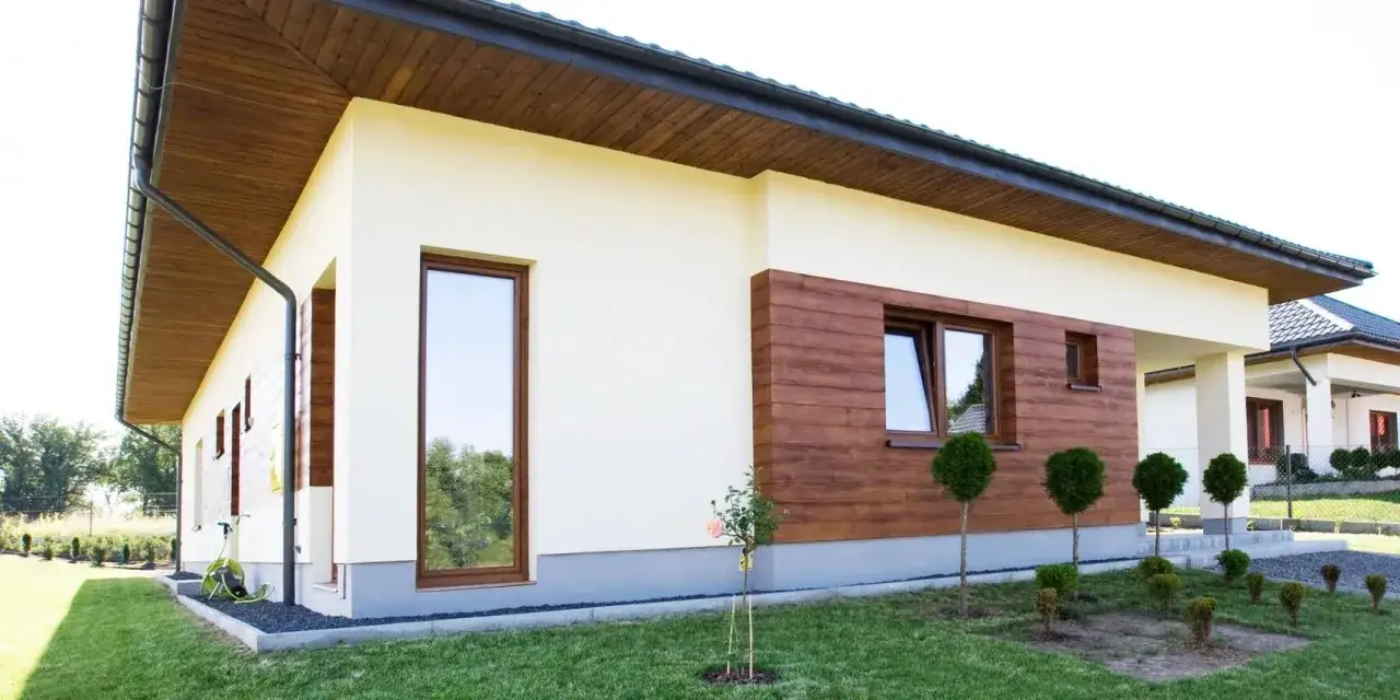 Nowoczesny dom z jasnym tynkiem silikonowym i drewnianą elewacją. Sprawdź cenę za m2 robocizny!