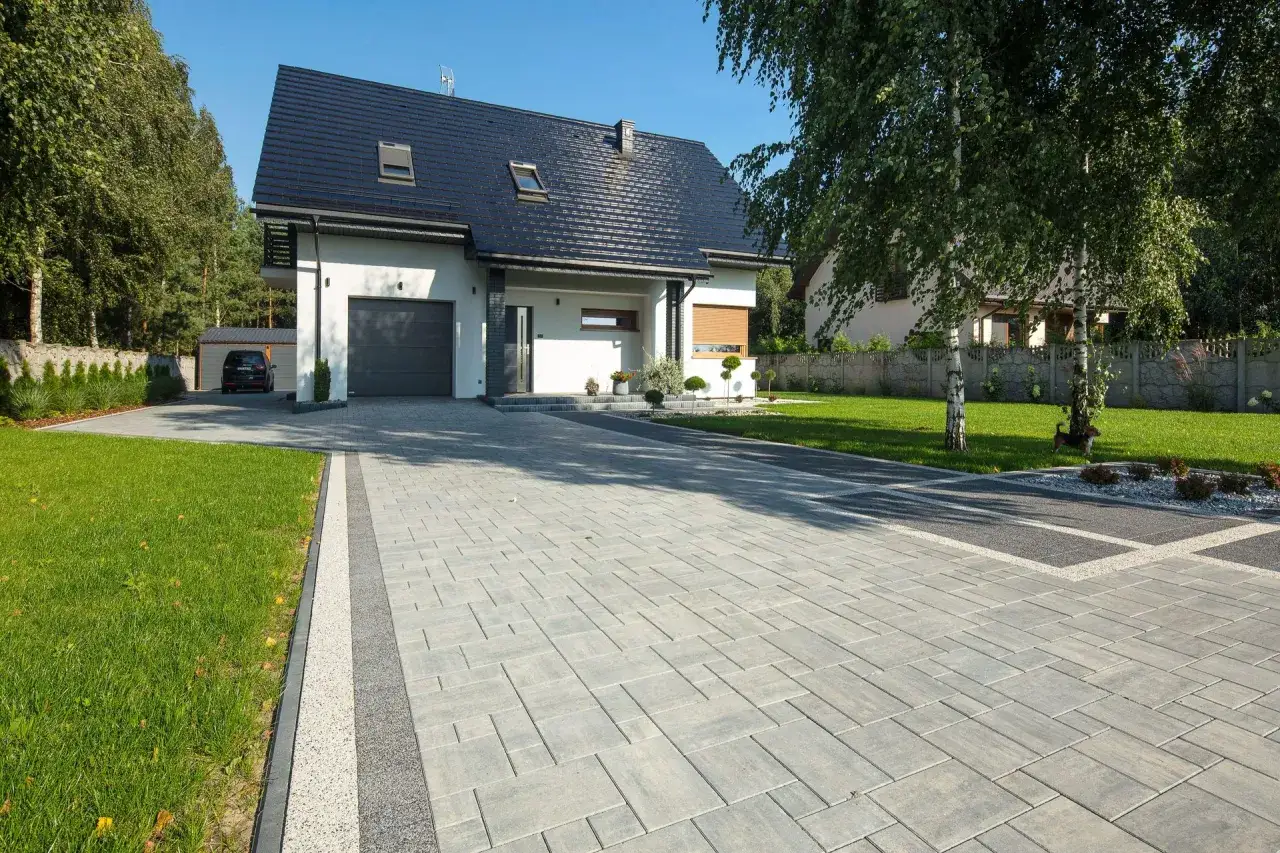 Nowoczesny dom z podjazdem z kostki brukowej. Zastanawiasz się, ile kosztuje metr kostki brukowej? Ten podjazd wygląda na wykonany z wysokiej jakości materiałów.