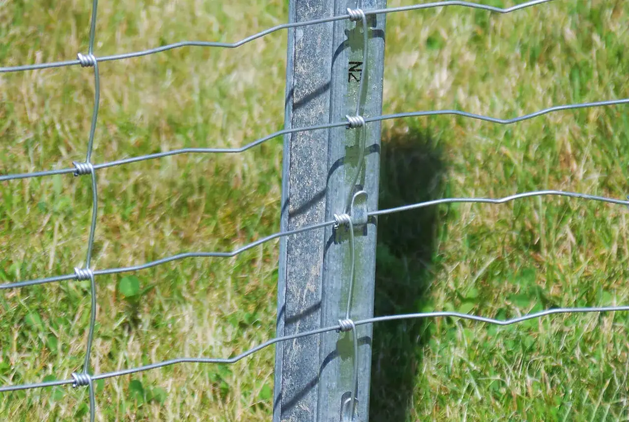 Szczegółowy montaż siatki ogrodzeniowej na metalowym słupku, z widocznym zapięciem drutu.