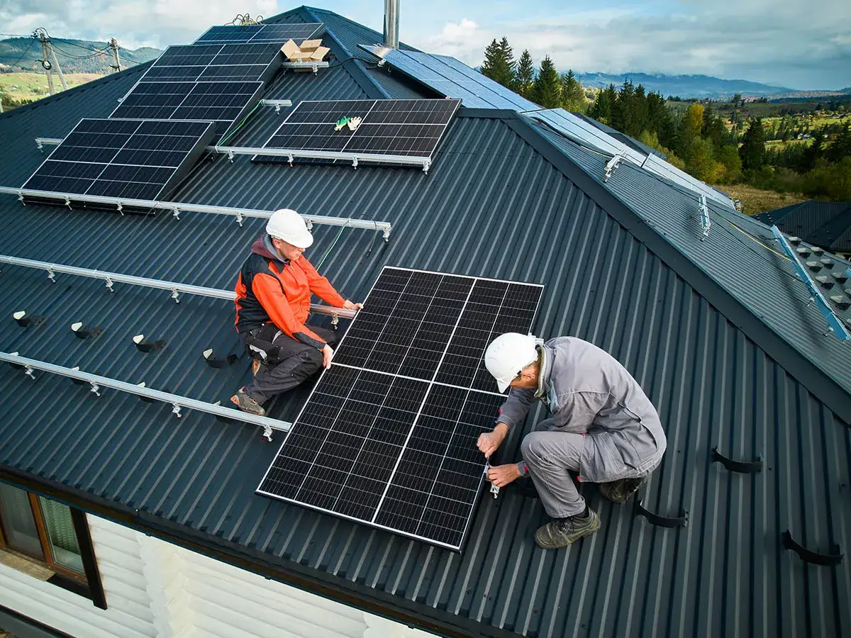 Dwóch pracowników przeprowadza montaż paneli fotowoltaicznych na dachu. Pracują nad instalacją, która zapewni czystą energię.