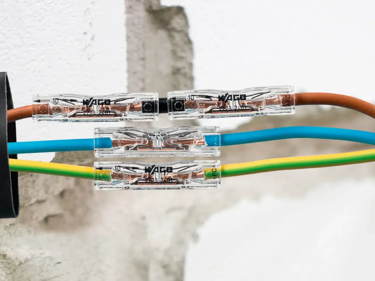Złączki Wago jak stosować: proste połączenie przewodów elektrycznych. Brązowy, niebieski i żółto-zielony kabel połączone w przezroczystych złączkach.