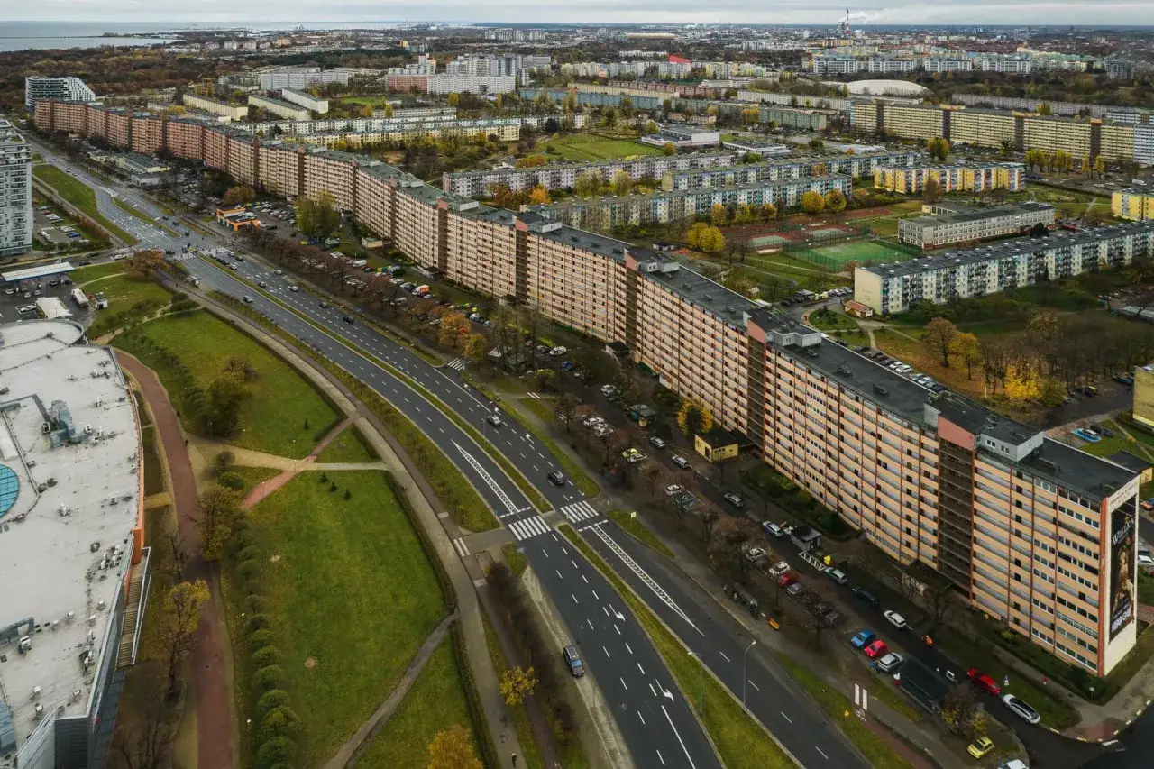 Najdłuższy blok w Polsce, falujący budynek mieszkalny z pomarańczową elewacją, otoczony zielenią i drogą z samochodami.