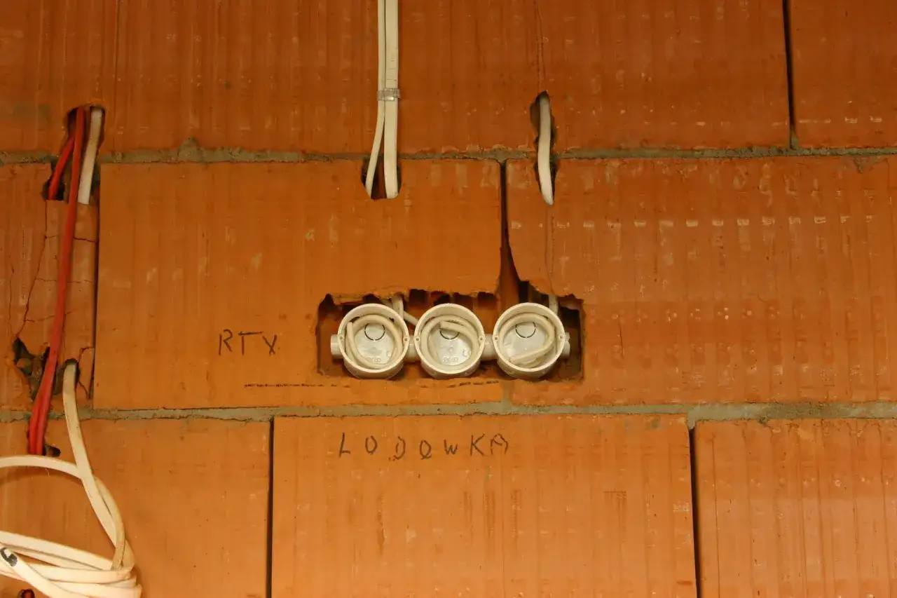 Instalacja elektryczna w budowie. Widoczne puszki instalacyjne i przewody. Napisy