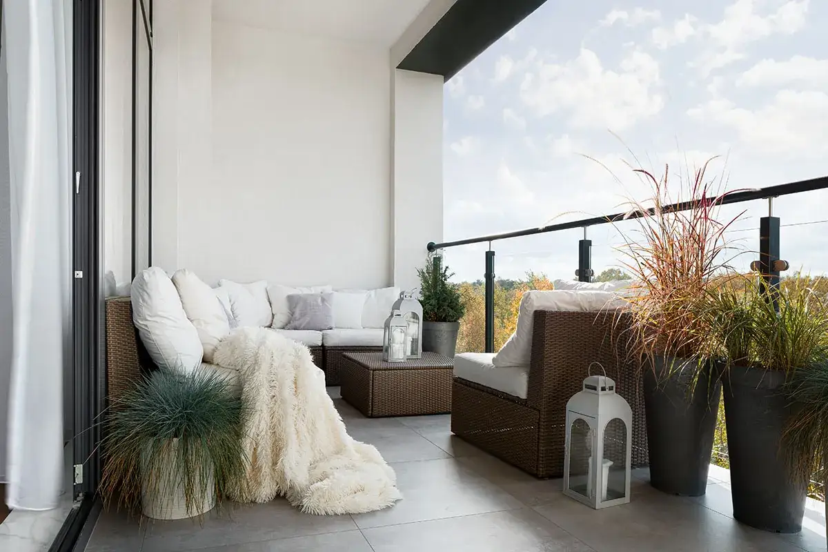 Przytulny balkon typu loggia z rattanowymi meblami, puszystym kocem i ozdobnymi latarniami.