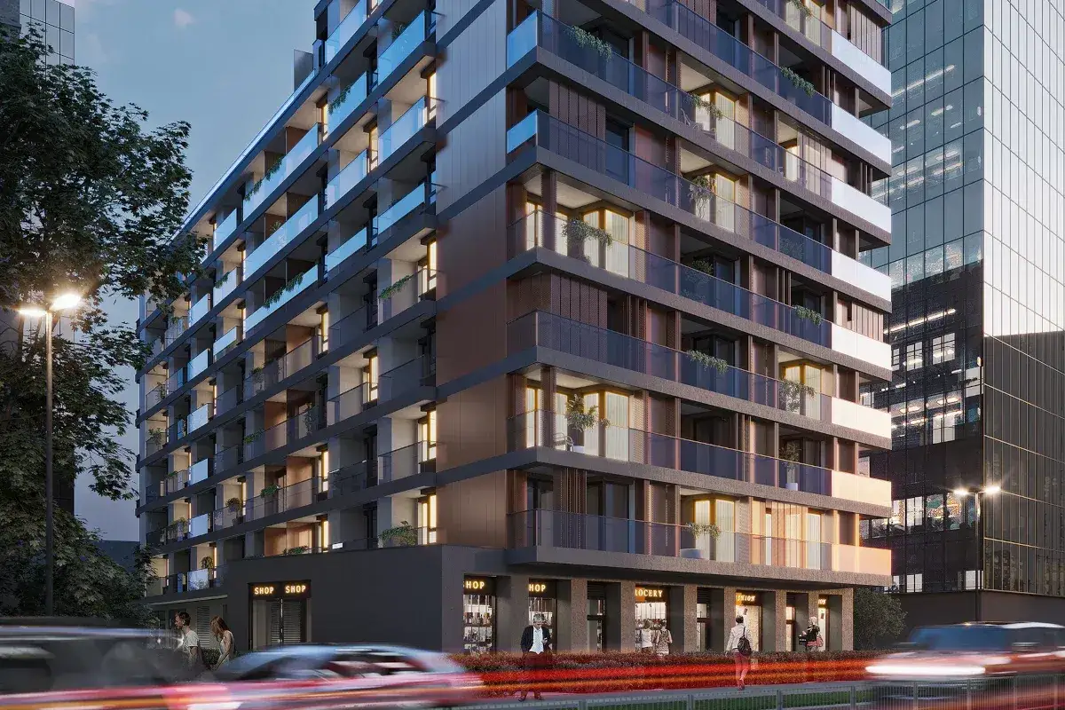 Nowoczesny apartamentowiec z przeszklonymi balkonami i sklepami na parterze, otoczony miejską zielenią i ulicznym ruchem.
