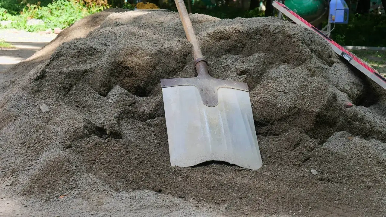 Duża hałda suchego betonu, łopata wbita w piasek. Cena 1m3 betonu zależy od składu.