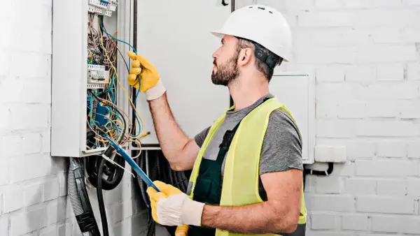 Elektryk w kasku i kamizelce odblaskowej pracuje przy skrzynce z przewodami. Dokładna wycena koszt instalacji elektrycznej wymaga precyzji.