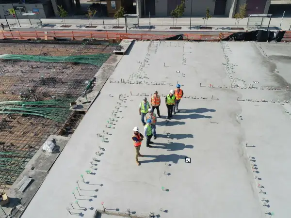 Grupa budowlańców na placu budowy. Widać zbrojenie i świeży beton. Sprawdzają beton b25 cena za m3.