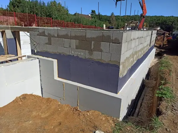 Izolacja fundamentów w starym domu w trakcie budowy. Ściany z bloczków betonowych, izolacja przeciwwilgociowa i termiczna.