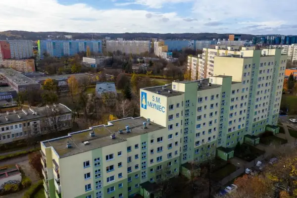 Osiedle bloków z wielkiej płyty S.M. Młyniec w jesiennej scenerii. Długie, wielopiętrowe budynki mieszkalne dominują w krajobrazie.
