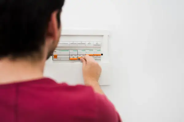 Mężczyzna manipuluje wyłącznikami w skrzynce elektrycznej, co może być pierwszym krokiem, by dowiedzieć się, jak obliczyć zużycie prądu.