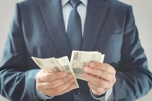 Mężczyzna w garniturze liczy banknoty 100 zł. Czy to jego zarobki jako członka rady osiedla?