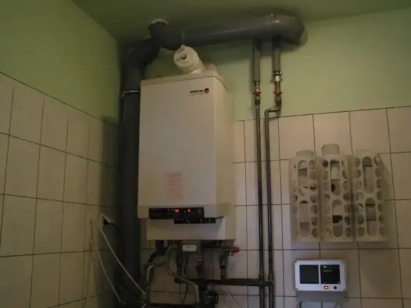 Kocioł gazowy gotowy na sezon grzewczy. W pomieszczeniu z kafelkami widać też termostat i uchwyty na papier toaletowy.