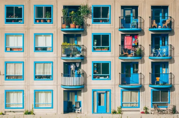 Elegancka loggia i balkon z niebieskimi ramami okiennymi, pełne zieleni i suszącego się prania, tworzą kolorowy wzór na fasadzie budynku.