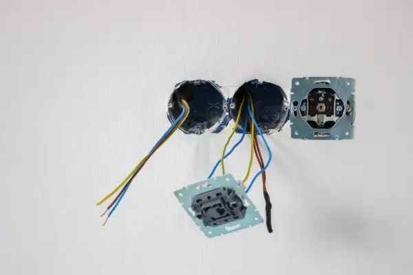 Osadzanie puszek elektrycznych w ścianie. Widać przewody wychodzące z dwóch puszek, a obok zamontowaną ramkę gniazdka.