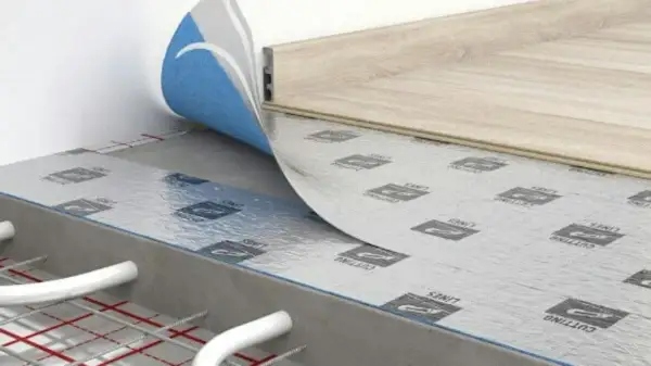 Warstwa izolacyjna pod panele laminowane, z folią aluminiową i niebieskim wykończeniem, na podłożu z ogrzewaniem podłogowym.