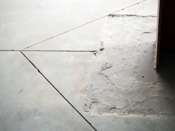 Widoczne pęknięcia i nierówności na posadzce betonowej, wskazujące na potrzebę wykonania dylatacji.