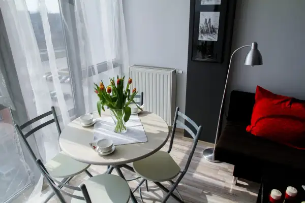Stół z tulipanami i filiżankami, obok kanapa z czerwoną poduszką. Idealne miejsce na poranną kawę w **garsonierze co to** za urok!